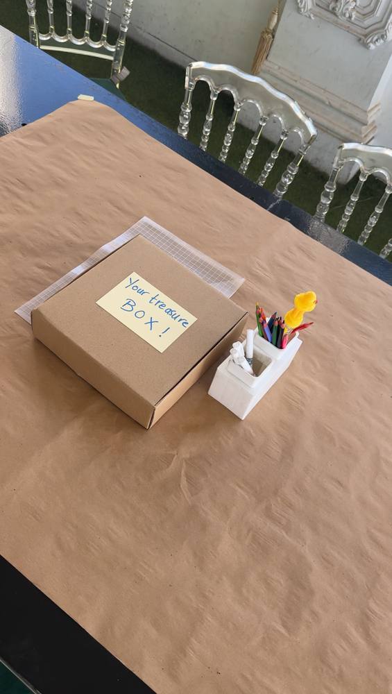 A kraft box labeled Your treasure box next to coloured pencils on a set table