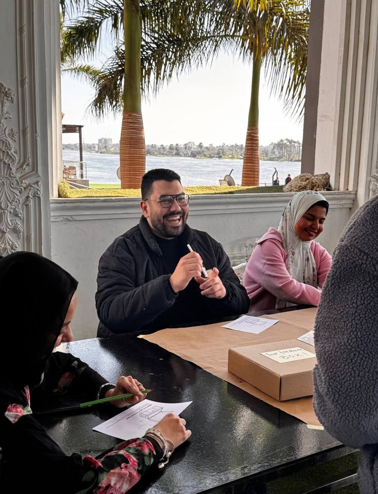 A participant laughing at a table set with kraft paper and a treasure box, the Nile behind him